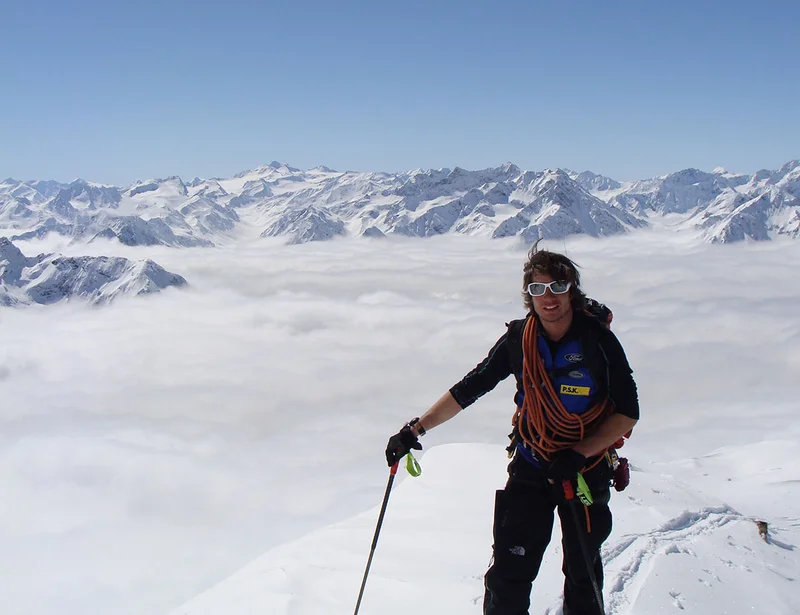 Bergführer mit Seil vor einem Nebelmeer und Alpenpanorama