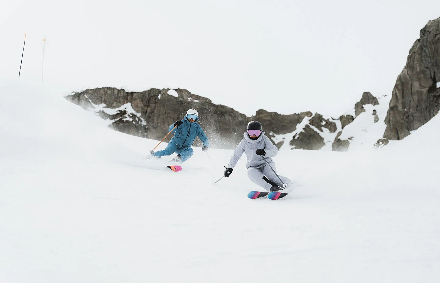 Zwei Skifahrerinnen beim Carving auf der Piste unter Felsen