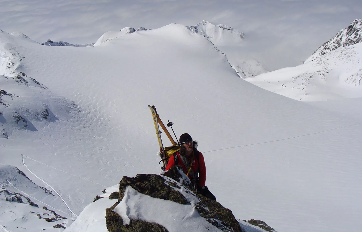 Bergsteiger mit Ski am Rucksack auf einem Felsgrat über dem Gletscher