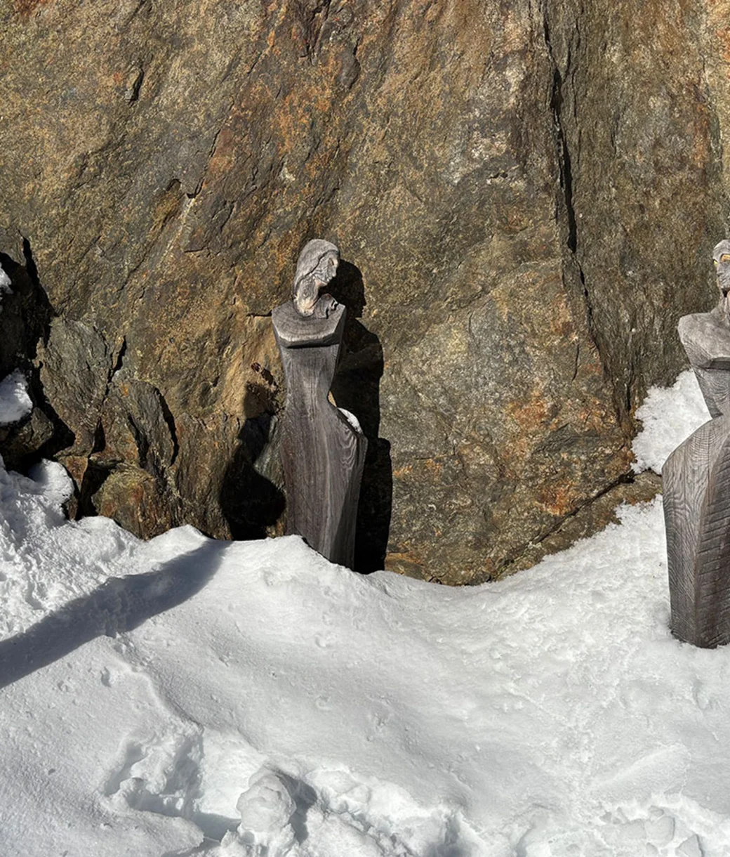 Holzskulpturen im Schnee vor einer Felswand